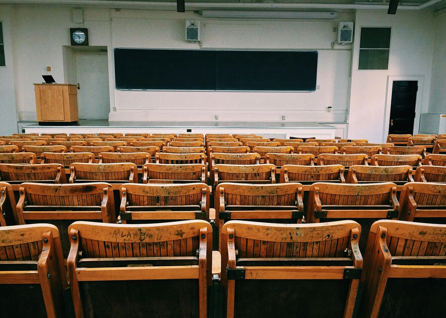 Prof. Dr. Marcus Mittenzwei - Hochschullehrer - Ein leerer Hörsaal mit Reihen von Holztischen für Studierende vor einer großen Tafel.